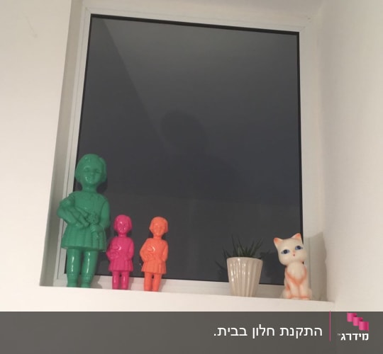 חלון אלומיניום עם פסלונים צבעוניים על אדן החלון